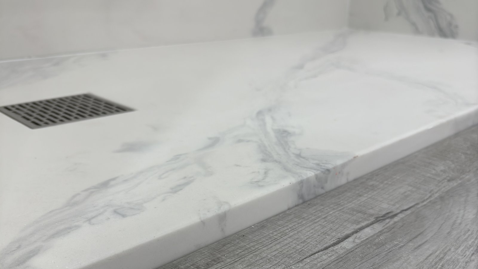 Cultured marble shower pan with veined Carrara finish and trench drain